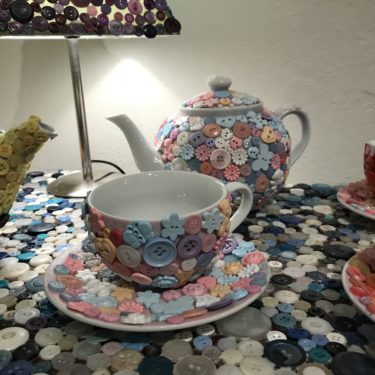 Close up image of artwork consisting of teapot and cup decorated with colourful buttons.