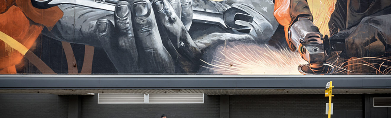 A man walks past a large mural that depicts metalwork in a car workshop