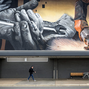 A man walks past a large mural that depicts metalwork in a car workshop