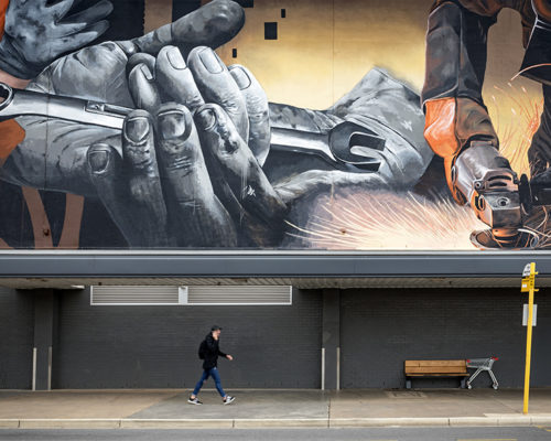 A man walks past a large mural that depicts metalwork in a car workshop